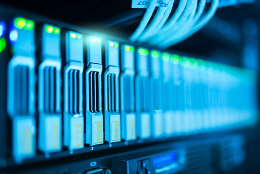 A cluttered server rack with blinking LEDs next to a laptop running redis-cli
