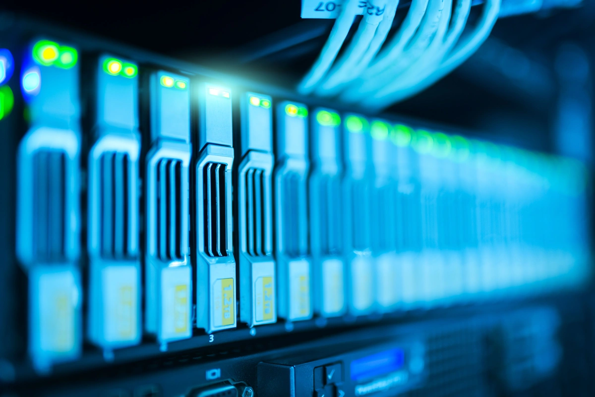 A cluttered server rack with blinking LEDs next to a laptop running redis-cli